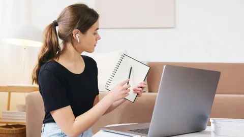 A learner wearing earbuds and using a notebook during an online session.